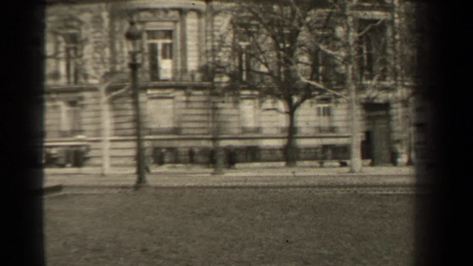 1947 Paris home-movie frame showing a stone facade, bare trees, street lamps, and a quiet boulevard edge.