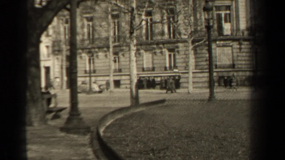 1947 Paris frame with distant pedestrians near a boulevard, bare trees, street lamps, and ornate stone building fronts.