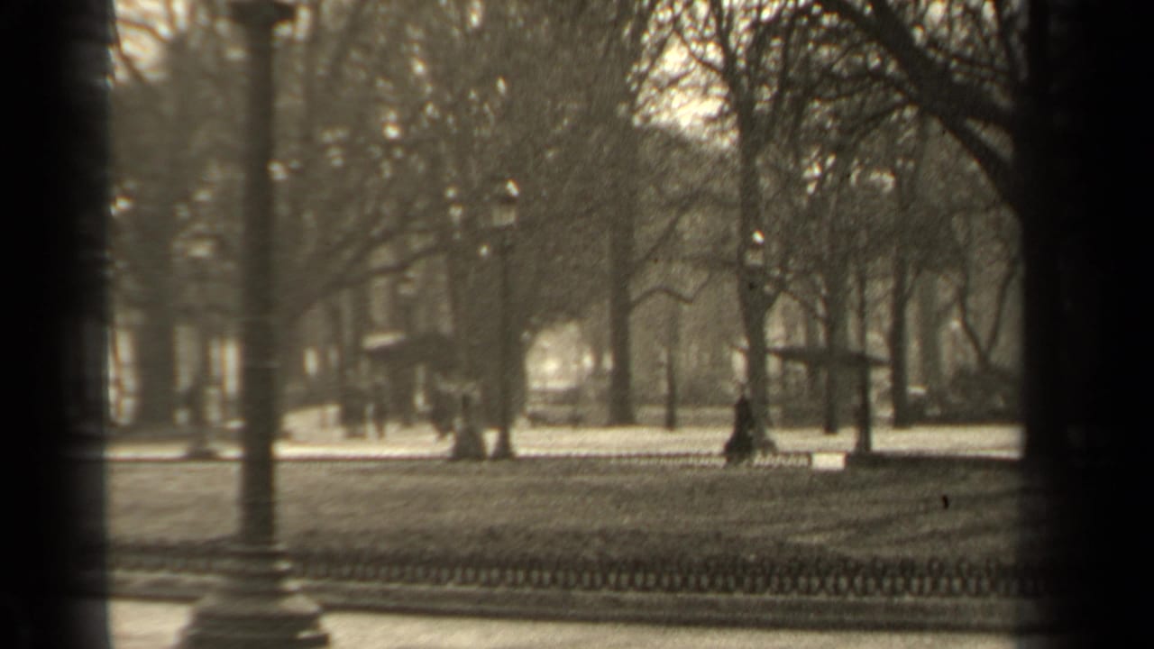 1947 Paris park-side view with bare trees, a low fence, street lamps, soft focus, and distant pedestrians.
