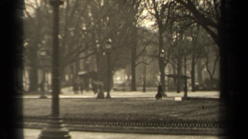 1947 Paris park-side view with bare trees, a low fence, street lamps, soft focus, and distant pedestrians.
