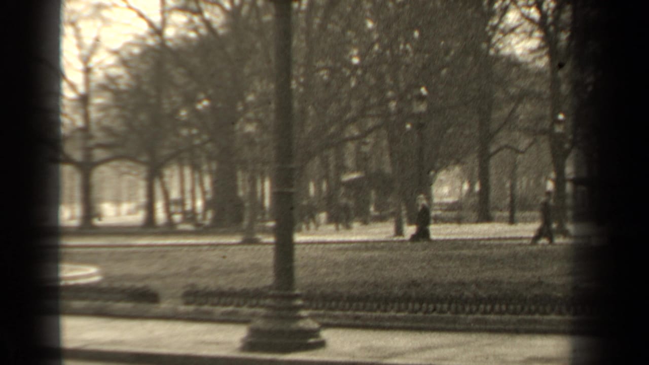 Park path seen past dark frame edges with trees, railings, and walkers.