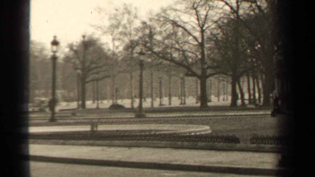 Paris park view from 1947 with a curved walkway, bare trees, lampposts, low fencing, and indistinct vehicles in the background.
