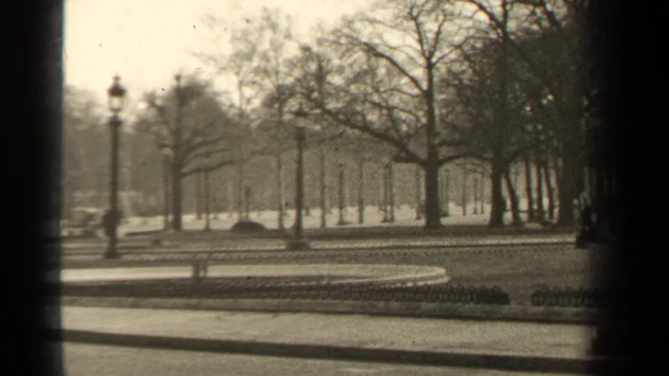 Paris park view from 1947 with a curved walkway, bare trees, lampposts, low fencing, and indistinct vehicles in the background.