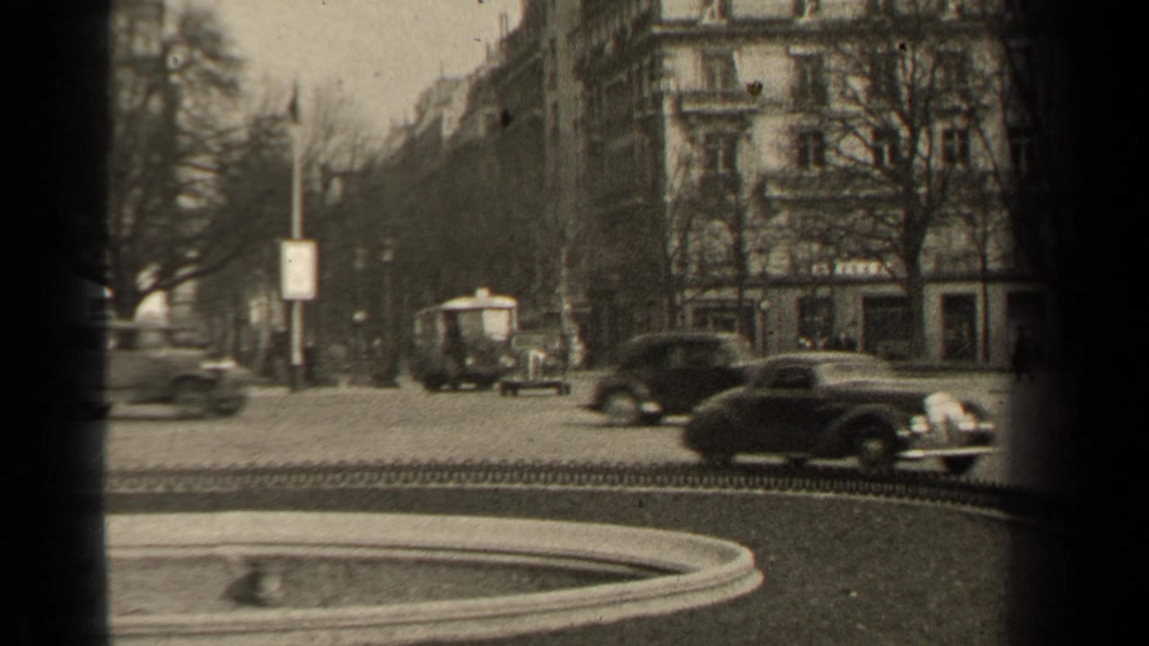 1947 Paris street view beside a park, with mid-century cars, a small vehicle, apartment facades, bare trees, and a curbside sign.