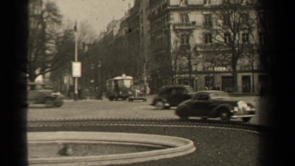 1947 Paris street view beside a park, with mid-century cars, a small vehicle, apartment facades, bare trees, and a curbside sign.