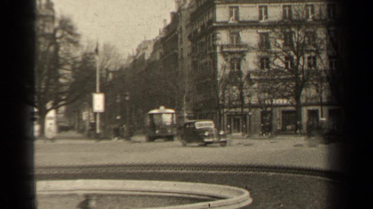 1947 Paris street view with mid-century cars, pedestrians, bare trees, ornate apartment buildings, and a dark 8mm frame edge.