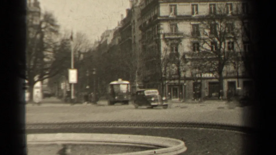 1947 Paris street view with mid-century cars, pedestrians, bare trees, ornate apartment buildings, and a dark 8mm frame edge.
