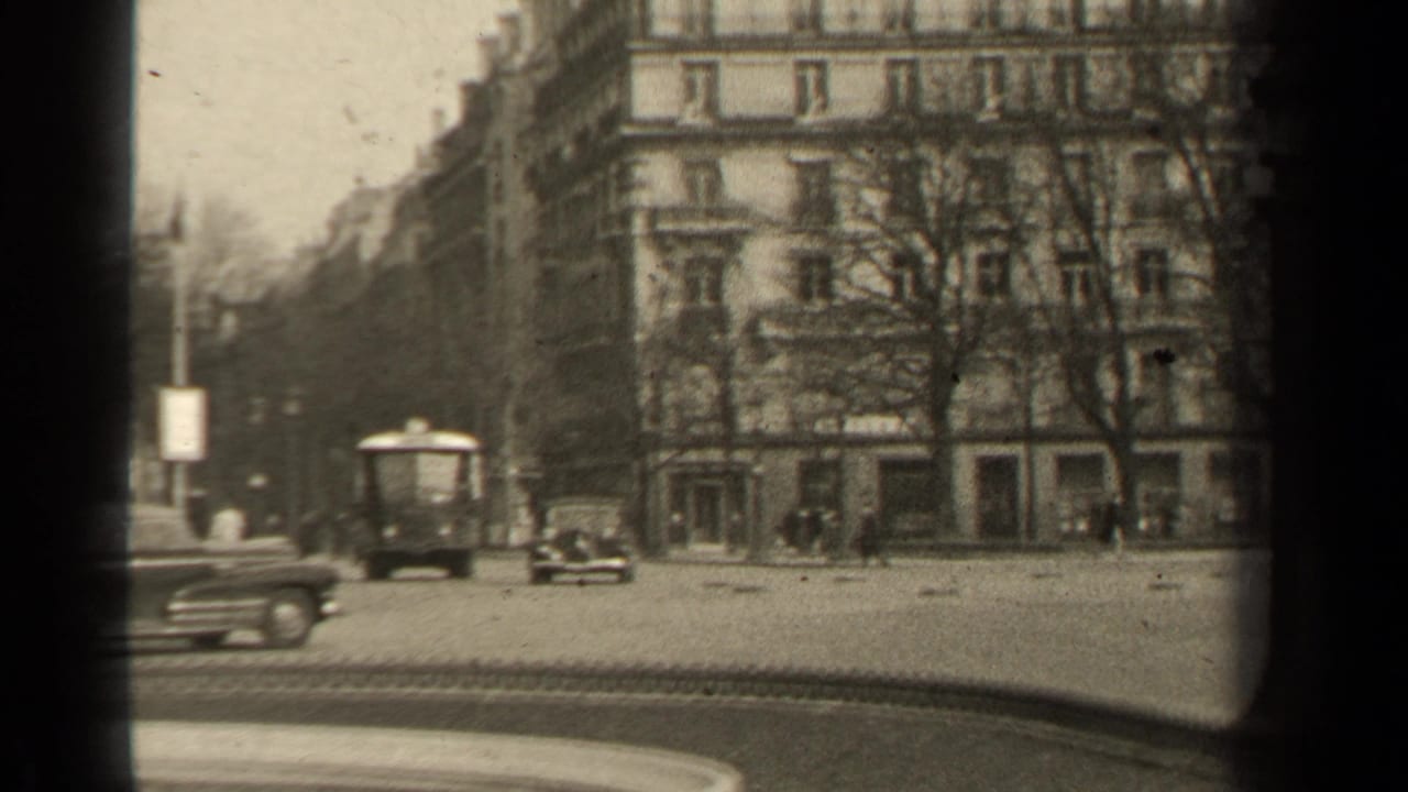 1947 Paris street view with a bus-like vehicle, cars, distant pedestrians, bare trees, and apartment facades framed by 8mm gate shadows.