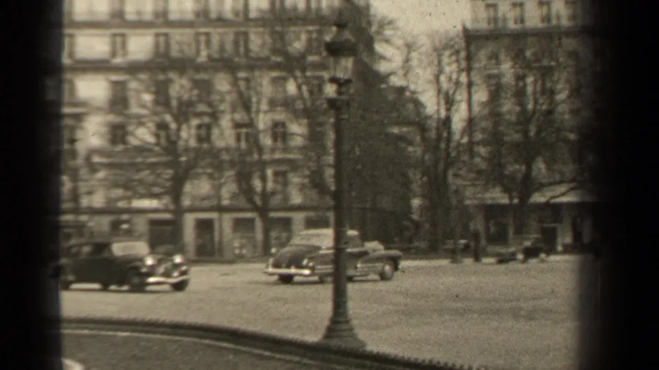 1947 Paris street view with classic automobiles, leafless trees, lampposts, and multi-story apartment facades in the background.