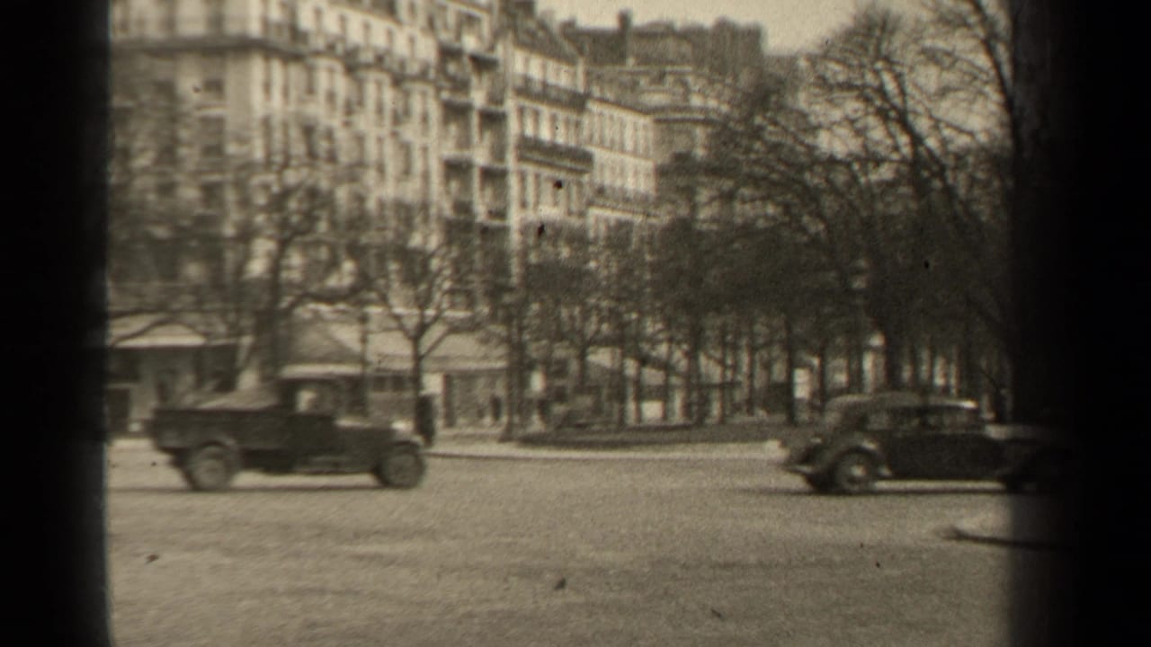 Paris street traffic in 1947, with two classic cars, leafless trees, storefronts, and residential buildings seen from a handheld home-movie viewpoint.
