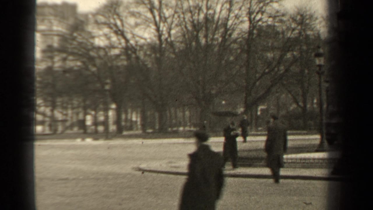 1947 Paris park view with bare trees, lampposts, distant pedestrians, and dark vertical frame bars in the foreground.