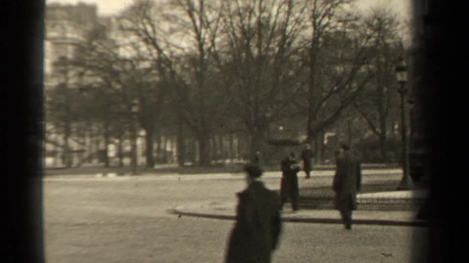 1947 Paris park view with bare trees, lampposts, distant pedestrians, and dark vertical frame bars in the foreground.