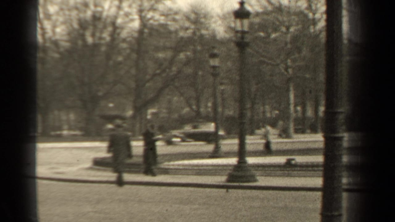 People walk near a park road with an older car visible in the background.