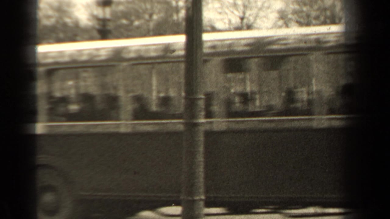 1947 Paris street view with a vintage bus moving past the park, partially obscured by poles and dark frame bars.