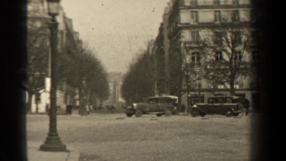 Paris boulevard scene from 1947 metadata, showing parked cars, apartment buildings, bare trees and a street lamp.