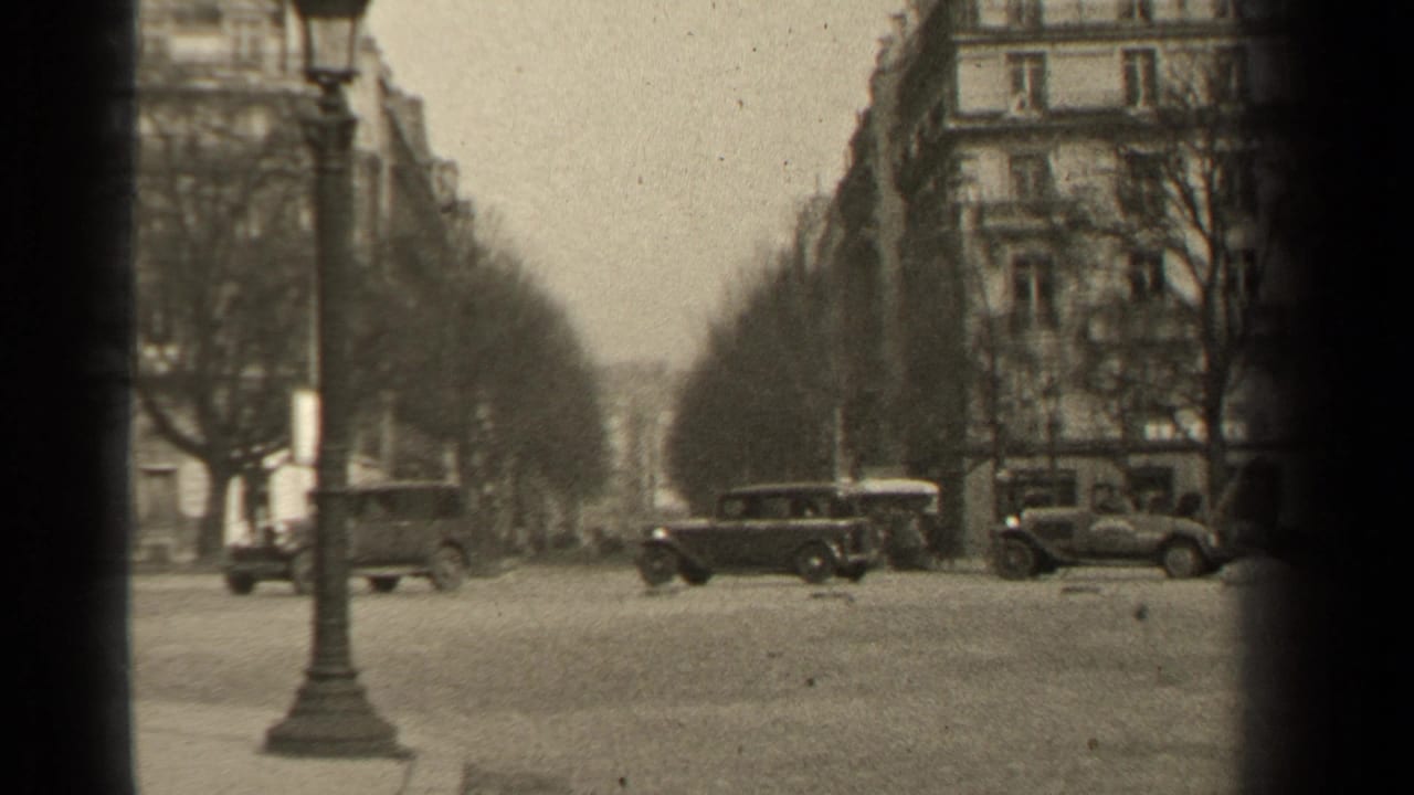 1947 Paris boulevard view with several automobiles crossing or parked near a lamppost and stone apartment blocks.