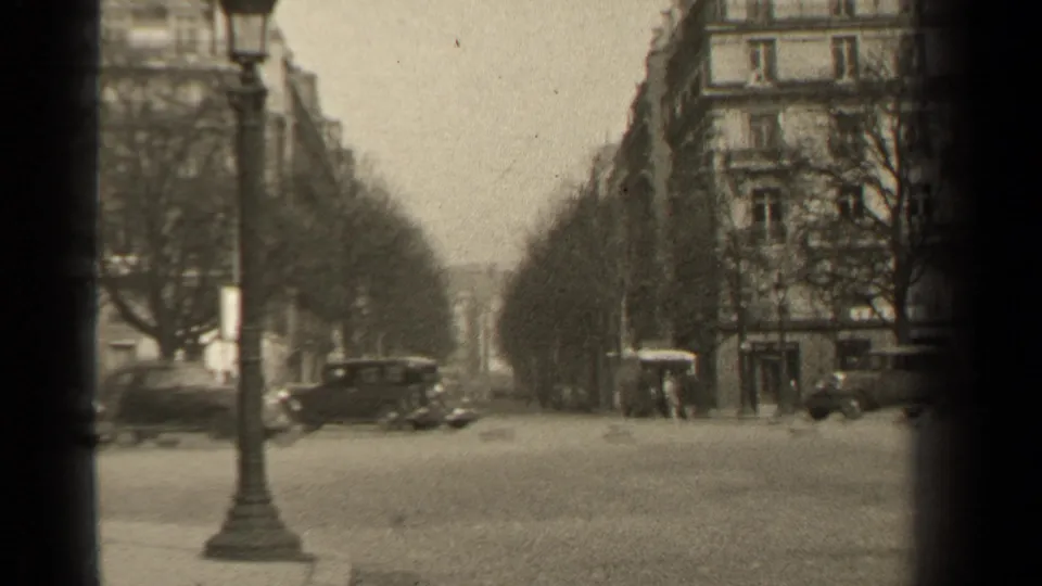 Paris boulevard scene from 1947 with cars near the curb, a lamppost, bare trees, and multi-story buildings in soft focus.