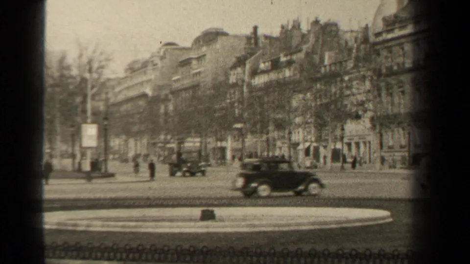 1947 Paris street view with period cars, pedestrians, bare trees, and stone building facades seen from an 8mm home-movie angle.
