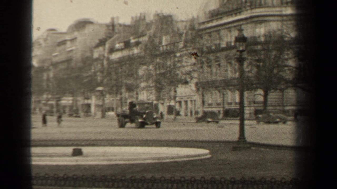 Paris street scene with multiple period vehicles, a lamppost, pedestrians, and rows of stone buildings recorded on black-and-white 8mm film.