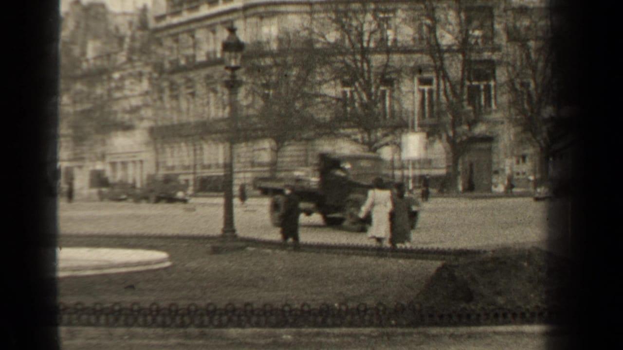 Paris street with pedestrians, a parked truck, classic cars, bare trees, and stone buildings.