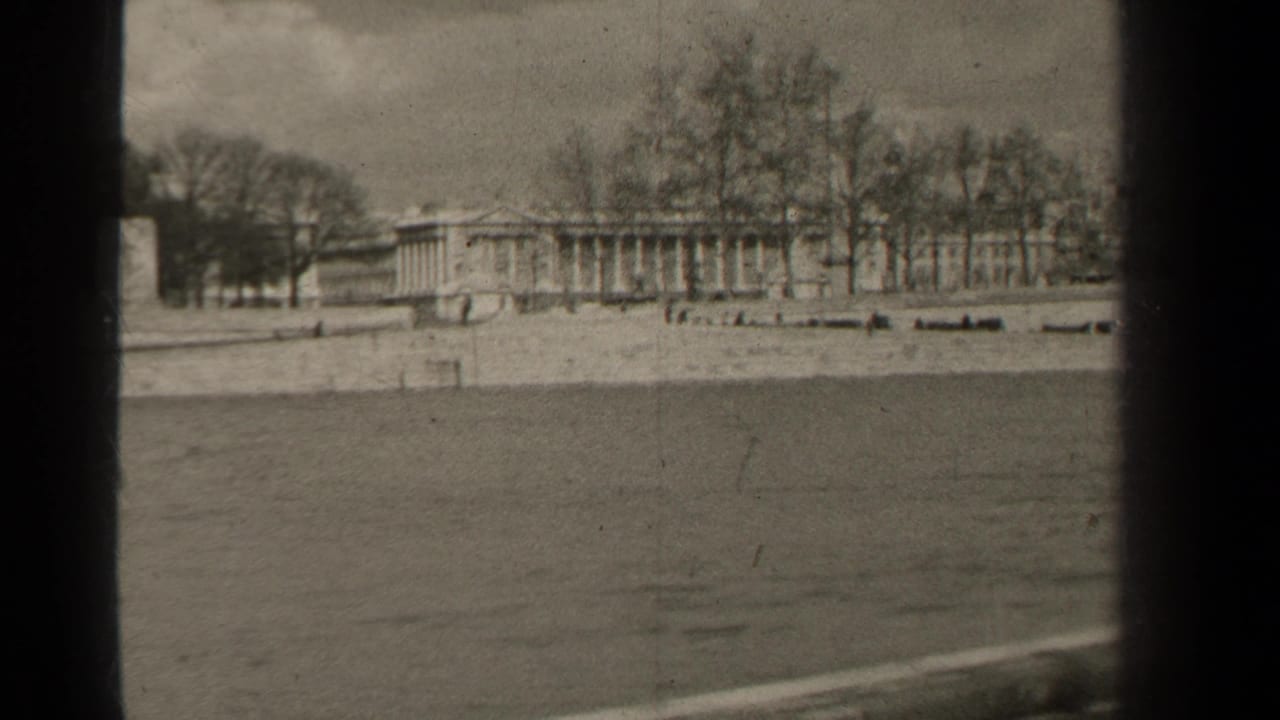 1947 Paris 8mm frame of a classical building behind leafless trees, seen from across a waterway with soft film grain.
