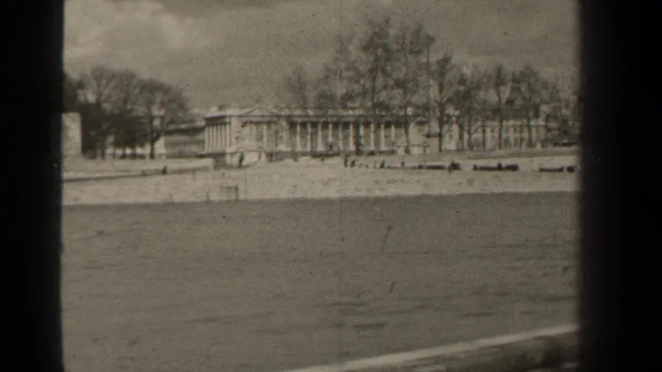 1947 Paris 8mm frame of a classical building behind leafless trees, seen from across a waterway with soft film grain.