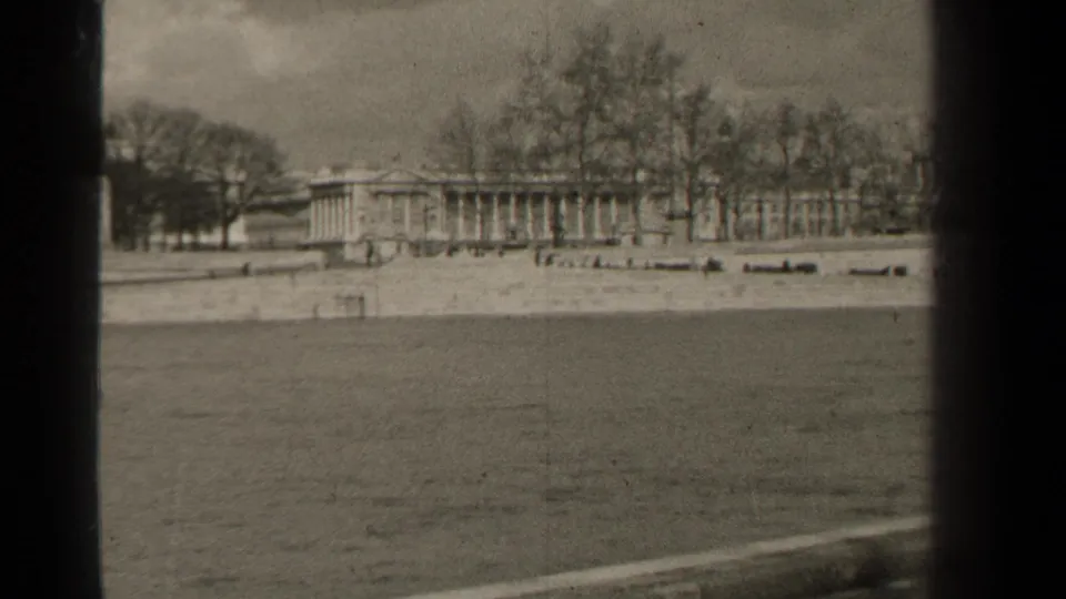 End frame of a 1947 Paris waterfront view, with a long columned building, bare trees, and dark 8mm frame borders.