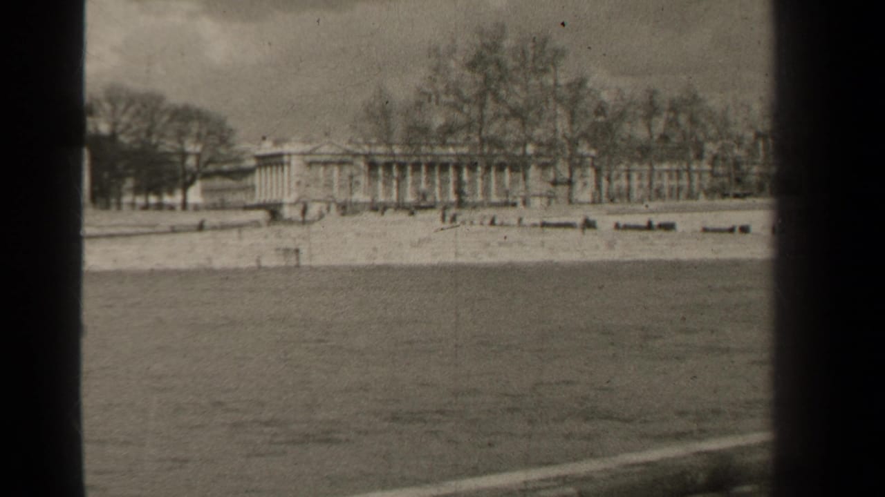 1947 Paris home-movie frame looking across open water toward a pale embankment, bare trees, and long classical buildings.