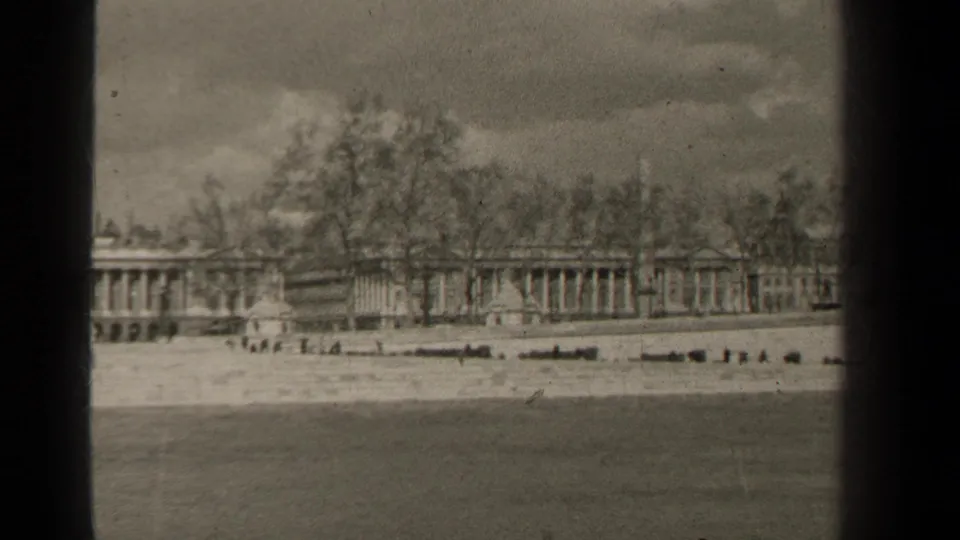 Black-and-white 1947 Paris frame showing distant pedestrians near a pale waterfront and long colonnaded buildings behind trees.