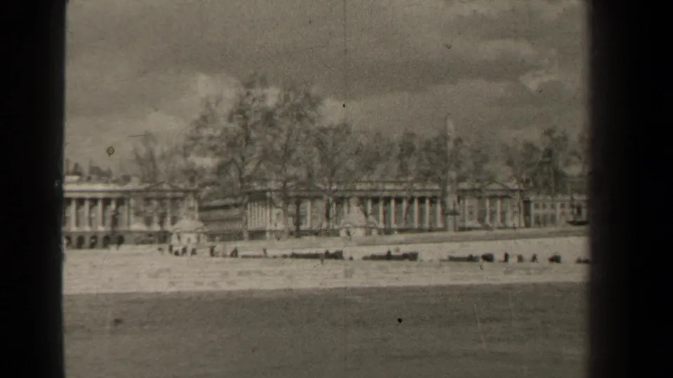 1947 Paris home-movie frame with a low waterfront, distant pedestrians, bare trees, and classical architecture in soft focus.
