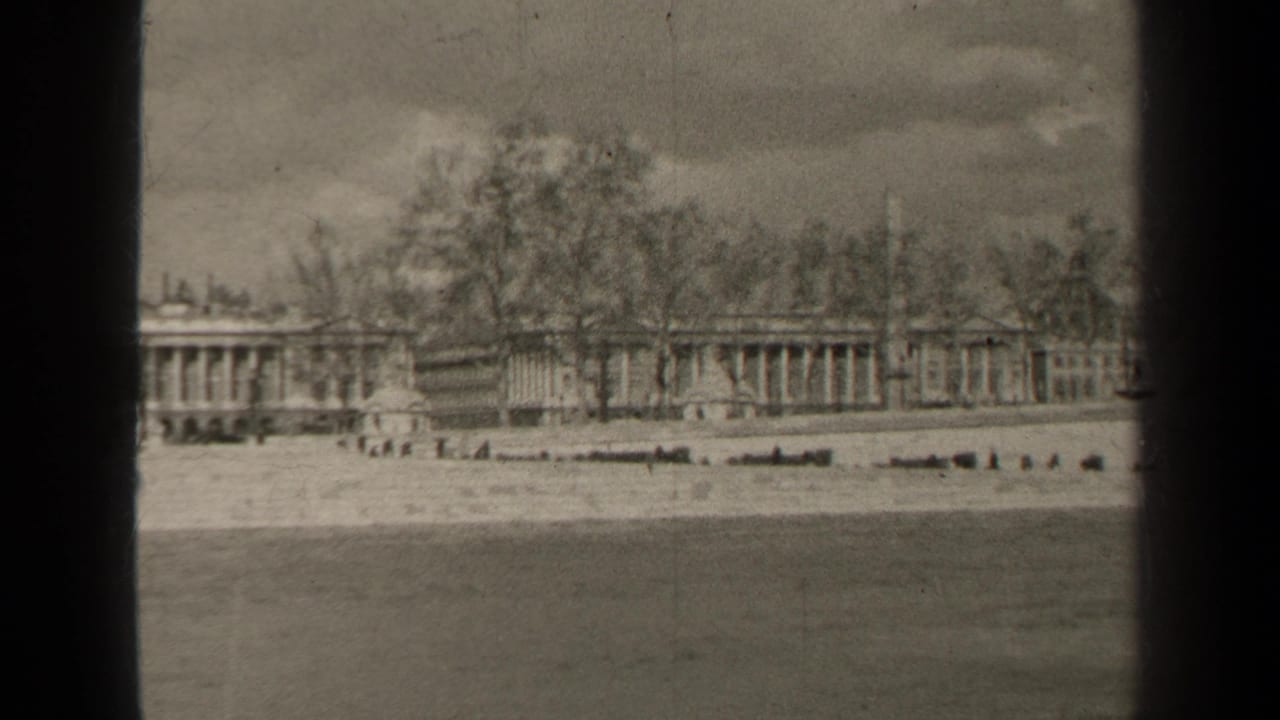1947 Paris home-movie frame showing water in the foreground, an embankment, bare trees, and a distant formal building complex.