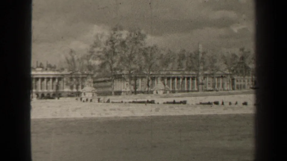 1947 Paris home-movie frame showing water in the foreground, an embankment, bare trees, and a distant formal building complex.