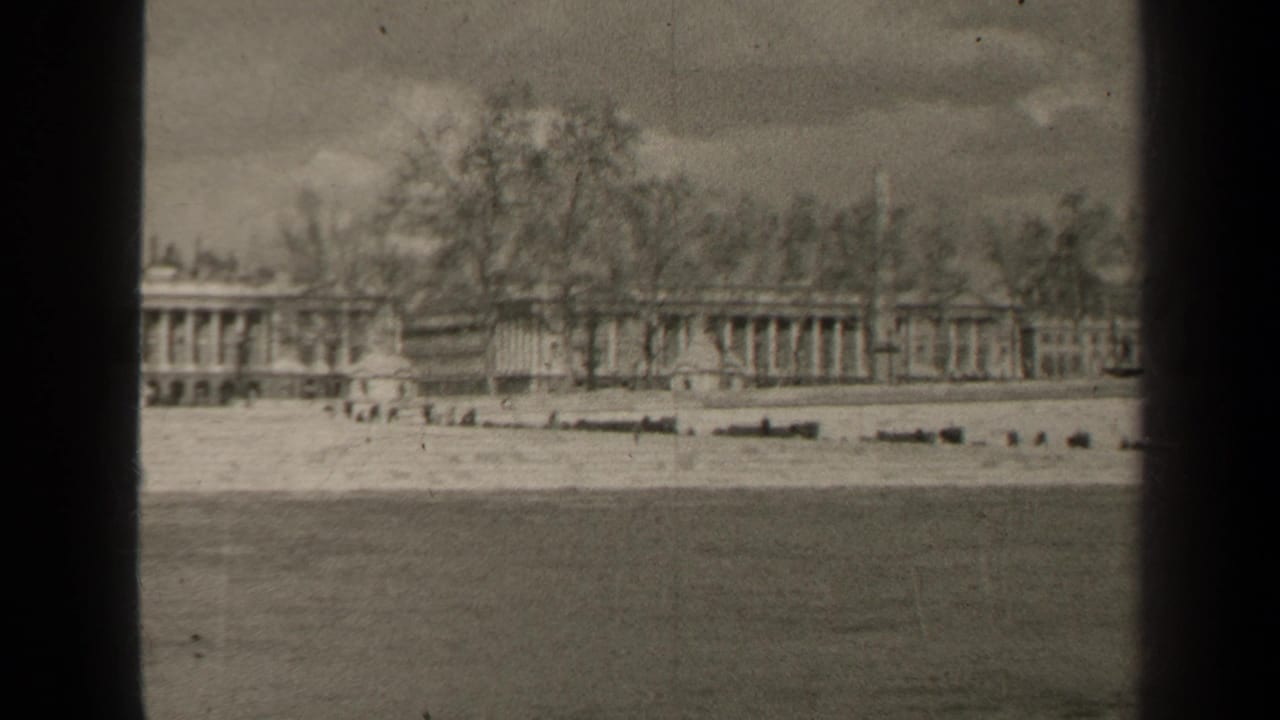1947 Paris home-movie frame showing a long columned building beyond the Seine, with bare trees and soft 8mm contrast.