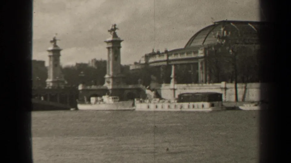 1947 home-movie frame of the Seine with a small boat passing below Pont Alexandre III pillars and the domed riverside structure.