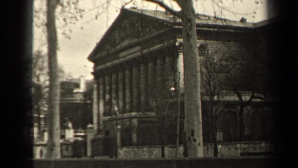 1947 Paris street-side view of a classical stone building with columns and a triangular pediment, partly framed by bare trees.