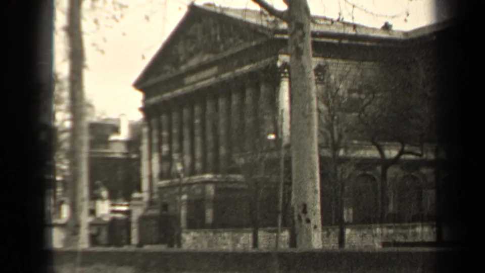 1947 Paris 8mm frame showing a classical building with columns, bare trees, sidewalk railing, and a quiet street.