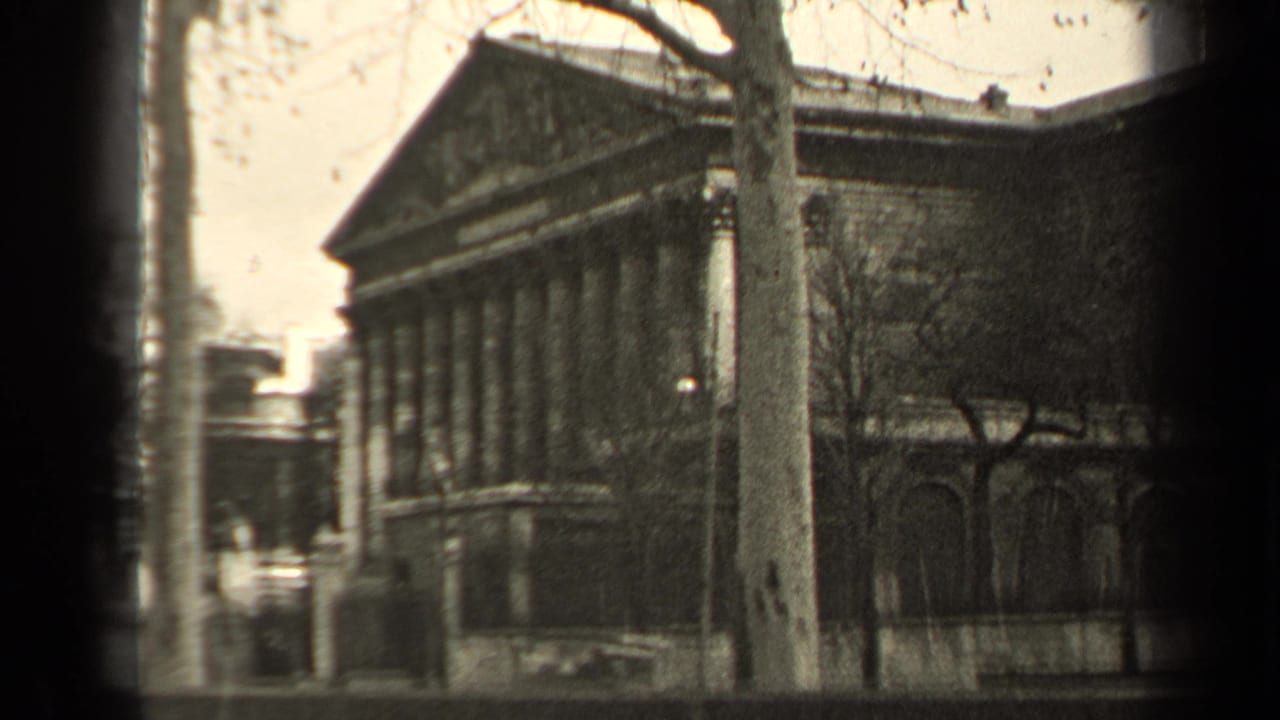 1947 Paris home-movie frame with a classical facade, bare trees, street foreground, and soft black-and-white film texture.