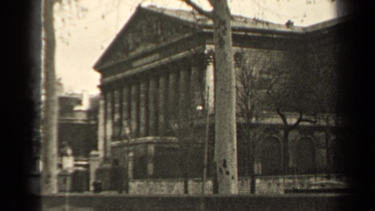 Classical building with columns and a triangular pediment beside a street and bare trees.