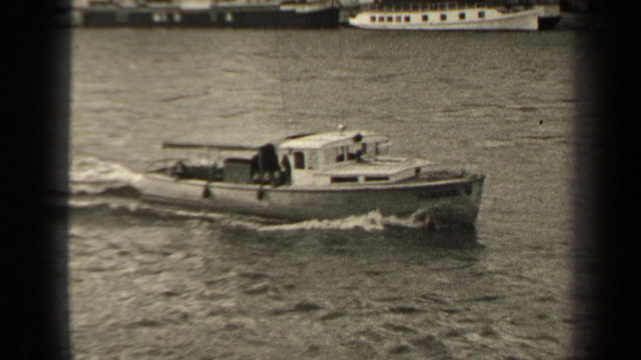 Small cabin motorboat moving across a river with wake and larger boats in the background.