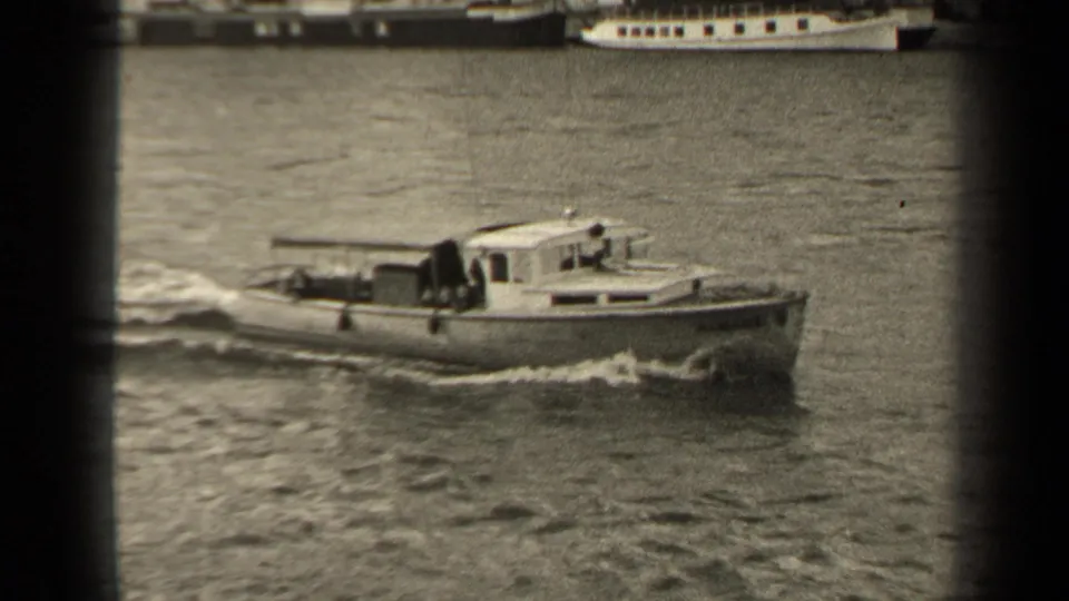 Black-and-white 1947 Paris river view with a small cabin motorboat crossing the water below distant moored vessels.