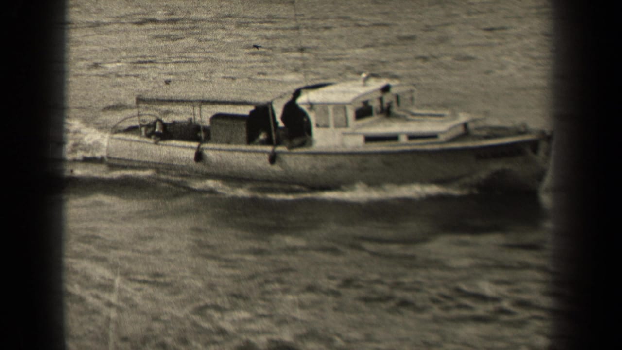 Small motorboat moves across choppy water, partly obscured by dark film-frame edges.