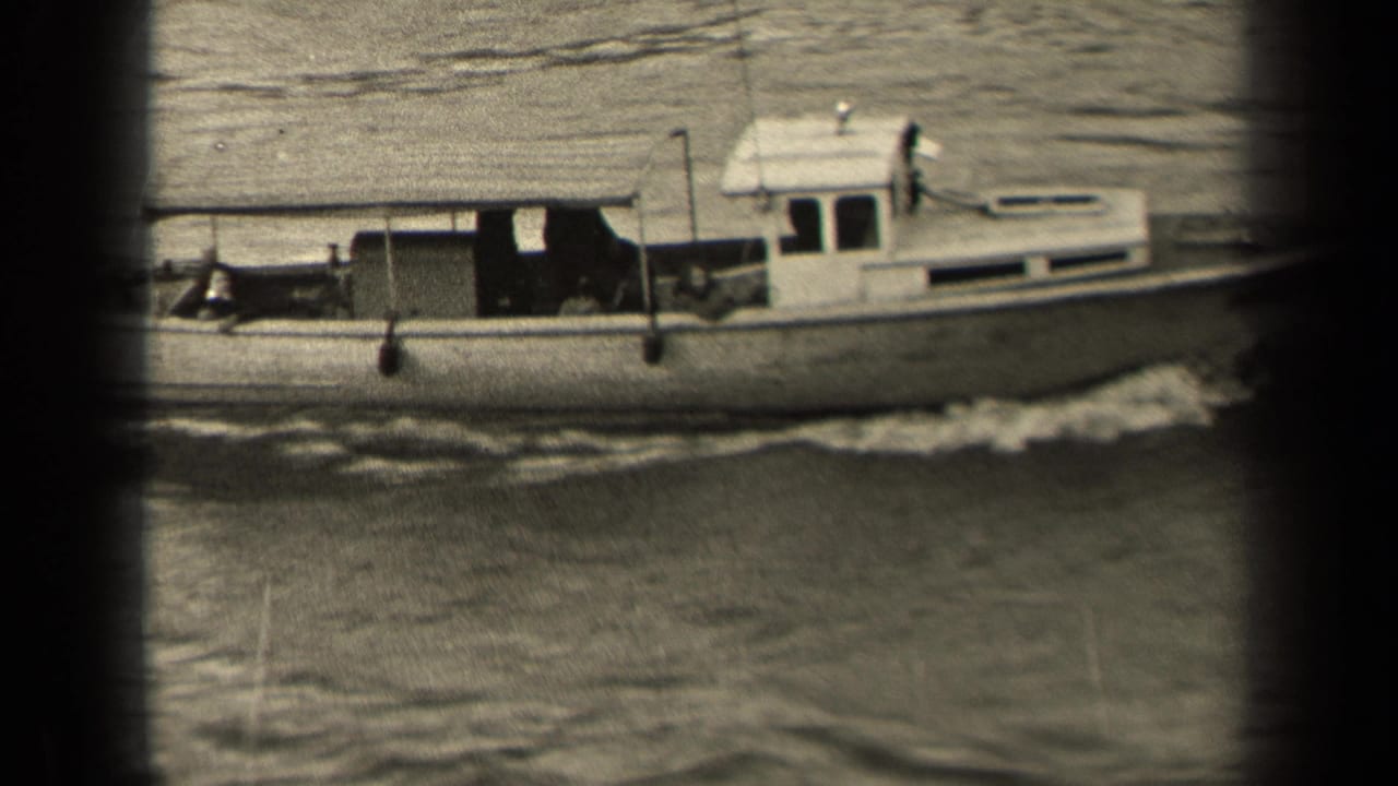 The cabin motorboat continues across frame, with people visible in shadowed areas aboard and a foamy wake trailing along the hull.