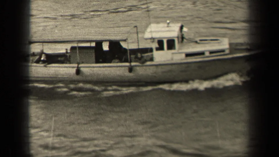 The cabin motorboat continues across frame, with people visible in shadowed areas aboard and a foamy wake trailing along the hull.