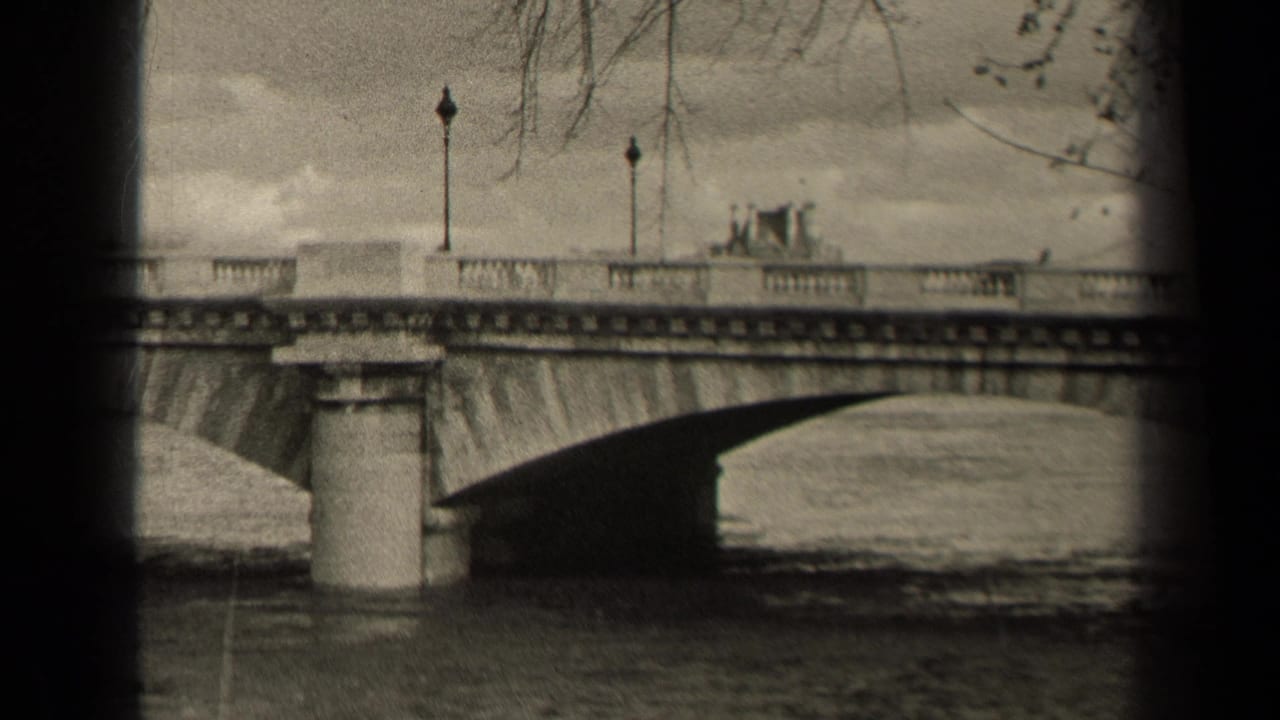 Stone arch bridge over water with lampposts, bare branches, and small traffic on the roadway.