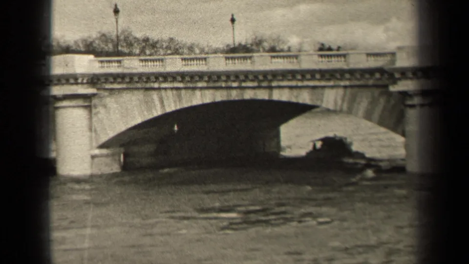 1947 Paris home-movie frame showing a stone bridge, river water, lampposts, and a small boat moving under the arch.