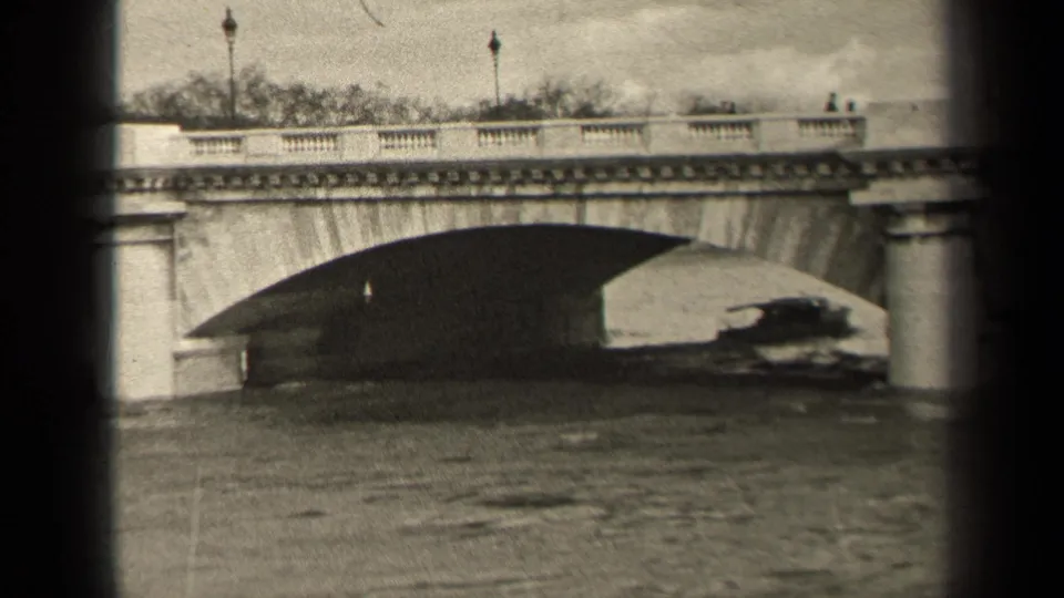 1947 Paris home-movie view of a small boat moving through the bridge shadow, with railings, lampposts, and pedestrians above.