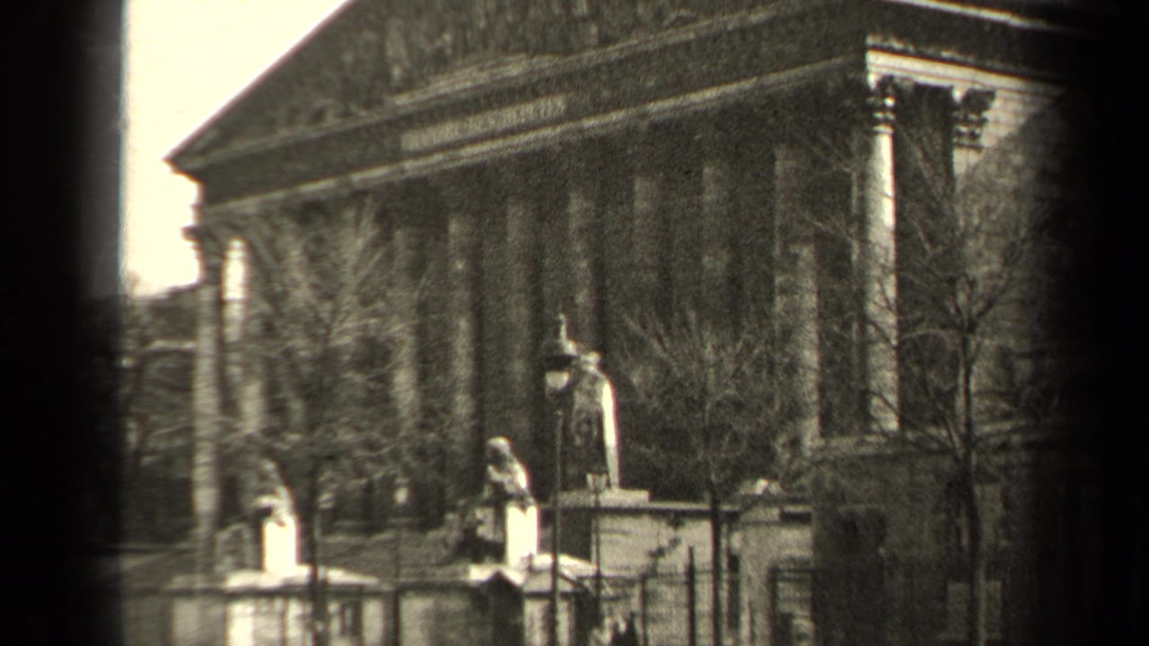 Columned neoclassical building with statues, bare trees, and fencing.