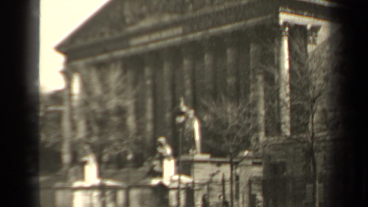 Soft 1947 Paris 8mm view of statues before a neoclassical columned building, partly obscured by trees and film edge shadow.
