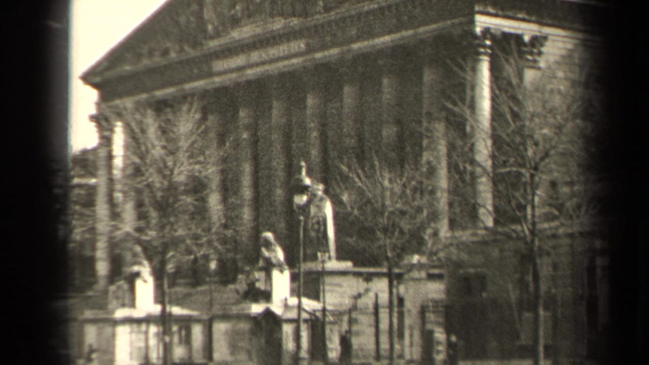 1947 Paris 8mm frame showing a columned civic building, foreground statues, leafless trees, and a fence.
