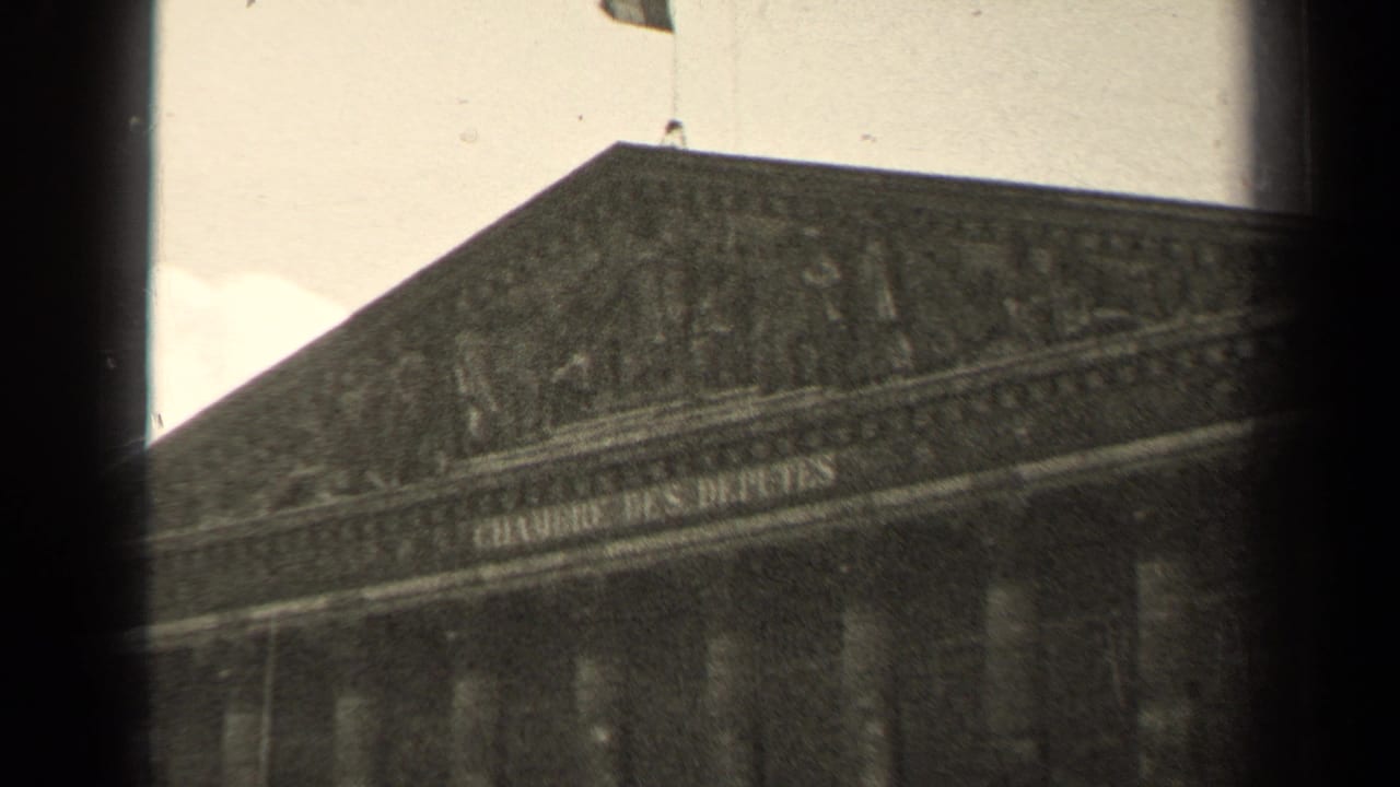 Facade inscription and roofline of the Palais Bourbon with a flag visible above.
